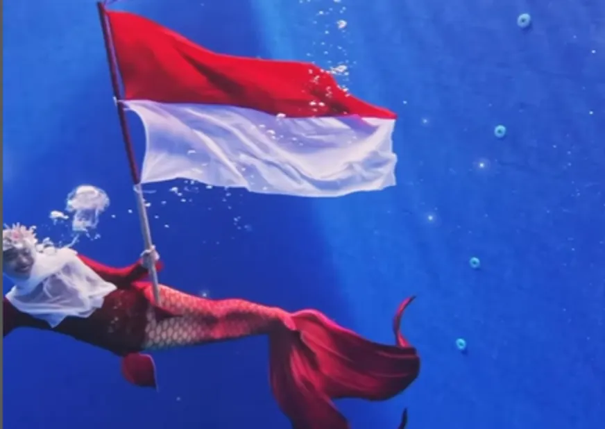Ria Ricis mengibarkan bendera merah putih dengan menggunakan busana ekor putri duyung berwarna merah.