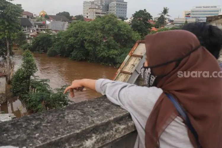 Warga menonton banjir dan aliran kali Ciliwung yang meluap dari atas Flyover Kalibata, Jakarta Selatan, Sabtu (20/2/2021). [Suara.com/Alfian Winanto]