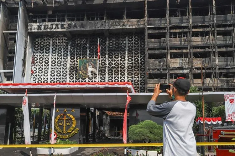 Seorang warga memfoto gedung utama Kejaksaan Agung RI yang habis terbakar di Jalan Sultan Hasanuddin, Jakarta Selatan, Minggu (23/8). [Suara.com/Alfian Winanto]