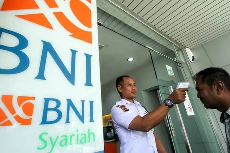 Petugas keamanan memeriksa suhu tubuh nasabah bank BNI Syariah Lhokseumawe, Aceh, Jumat (13/3/2020). (ANTARA FOTO/Rahmad/Tirto.id)