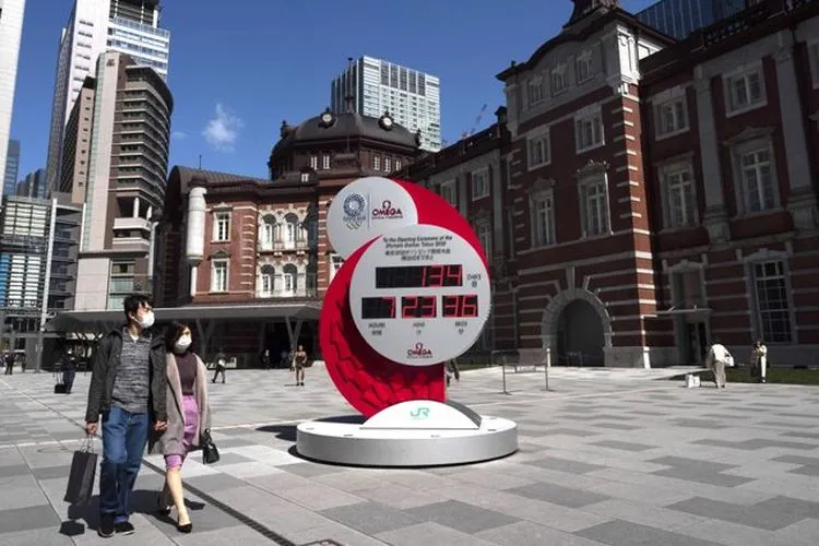 Warga Jepang mengenakan masker berjalan melewati jam hitung mundur Olimpiade di Tokyo, Jepang. (AFP/Kazuhiro Nagi)