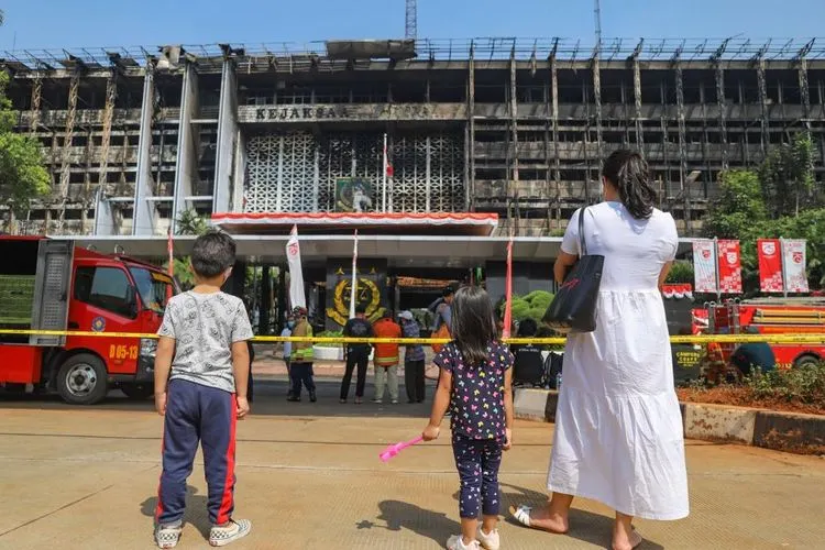 Seorang ibu membawa anak-anaknya untuk melihat gedung utama Kejaksaan Agung RI yang habis terbakar di Jalan Sultan Hasanuddin, Jakarta Selatan, Minggu (23/8). [Suara.com/Alfian Winanto]