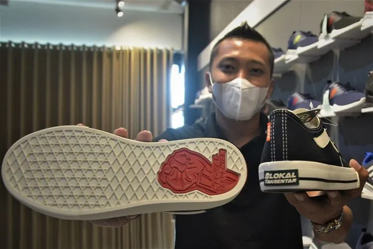 Aditya Caesarico menunjukkan sol sepatu bertuliskan #LokalTakGentar dengan genggaman tangan. Sepatu ini dijual dengan harga Rp99.900 per pasang. (Ayojakarta/Budi Cahyono)
