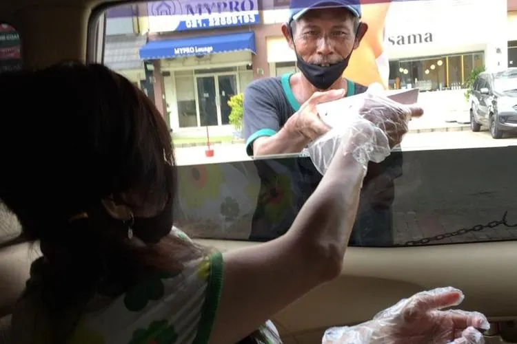 Salah satu donatur Gerakan Berbagi Kasih asal Paroki Santa Imaculata Citra Garden, Lucie  membagikan kotak makanan siap saji kepada warga, Kamis (16/4/2020)