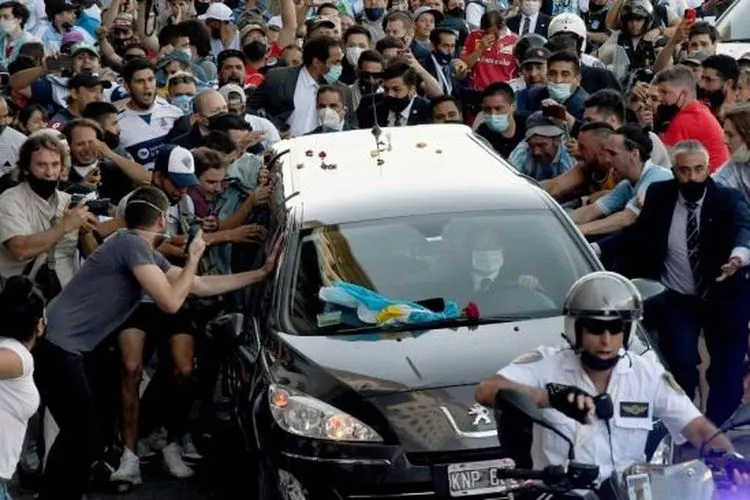 Foto yang dirilis Telam menunjukkan para penggemar berkerumun di samping mobil jenazah yang membawa mendiang legenda sepak bola Argentina Diego Armando Maradona dalam perjalanan dari istana kepresidenan Casa Rosada ke pemakaman Jardin Bella Vista, di Buenos Aires pada Kamis (26/11/2020) waktu setempat. [Raul FERRARI / TELAM / AFP]
