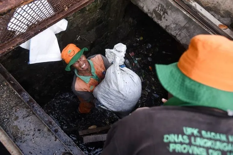 Petugas Dinas Lingkungan Hidup Pemprov DKI Jakarta mengangkat karung berisi lumpur dan sampah dari dalam salur air. (Facebook Anies Baswedan)