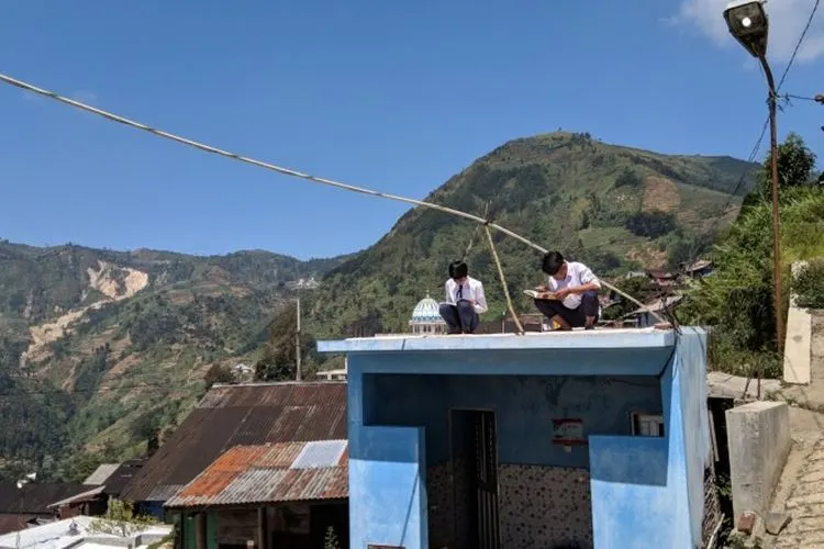 Dua orang siswa SMPN 4 Bawang saat menggunakan jaringan internet gratis yang dipasang sekolah dengan naik atap rumah. (Dok)