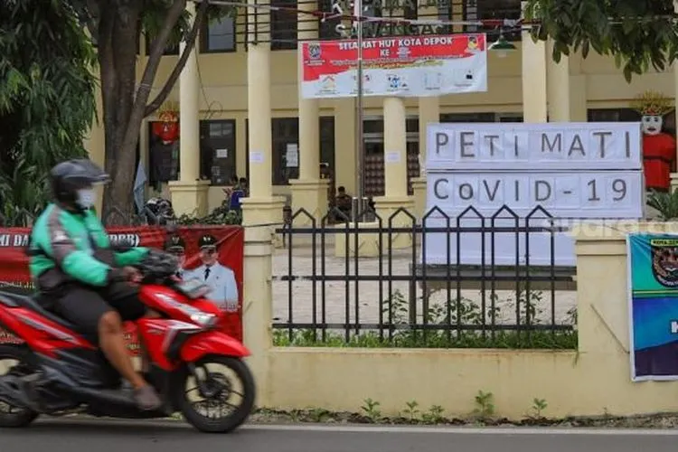 Pengemudi ojol melintas di depan peti mati Covid-19 di Kantor Kecamatan Sawangan, Depok, Jawa Barat, Senin (1/6). [Suara.com/Alfian Winanto]