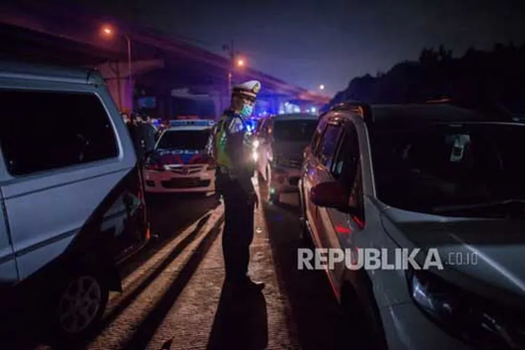 Petugas kepolisian mengarahkan kendaraan pribadi untuk keluar di Gerbang Tol Cikarang Barat, Bekasi, Jawa Barat, Sabtu (23/5) dini hari. Sekitar 200 pemudik yang menggunakan jasa travel tanpa izin beserta kendaraan pribadi terkena razia penyekatan dan akan dikembalikan ke Jakarta (Foto: Republika/Thoudy Badai )