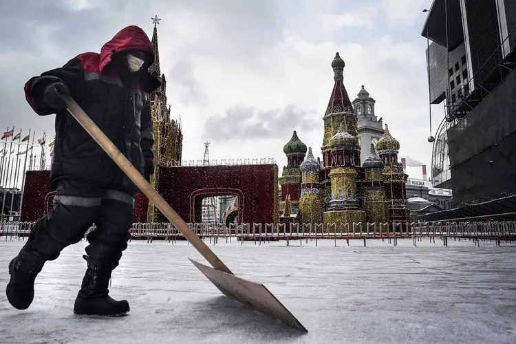 Seorang pekerja menggunakan masker medis membersihkan salju di depan replika Katedral St Basil di Moskow, 7 Februari 2020. AFP via Getty Images/Alexander Nemenov