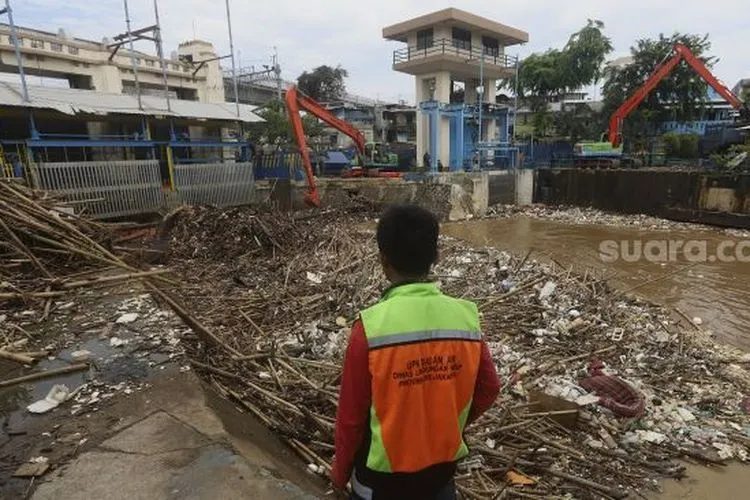 Petugas UPK Badan Air Dinas Lingkungan Hidup Provinsi DKI Jakarta dibantu alat berat mengangkat sampah kayu yang menumpuk di pintu air Manggarai, Jakarta, Selasa (22/9/2020). [Suara.com/Angga Budhiyanto]