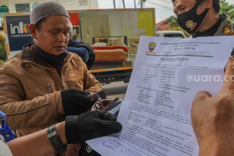 Petugas memeriksa Surat Izin Keluar Masuk (SIKM) bagi kendaraan bermotor dengan pelat nomer daerah yang akan memasuki Jakarta di Check Point PSBB Jalan Raya Kalimalang, Jakarta Timur, Rabu (27/5/2020). [Suara.com/Alfian Winanto]