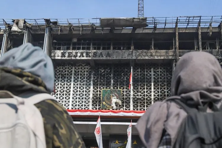 Dua orang warga melihat gedung utama Kejaksaan Agung RI yang habis terbakar di Jalan Sultan Hasanuddin, Jakarta Selatan, Minggu (23/8). [Suara.com/Alfian Winanto]