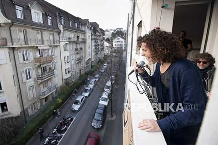 Penyanyi berkebangsaan Swiss Amandine (Rapin) melakukan konser singkat di balkonnya saat diberlakukannya keadaan darurat wabah penyakit corona di Lausanne, Swiss, Sabtu (28/3). (Foto: EPA-EFE/LAURENT GILLIERON)