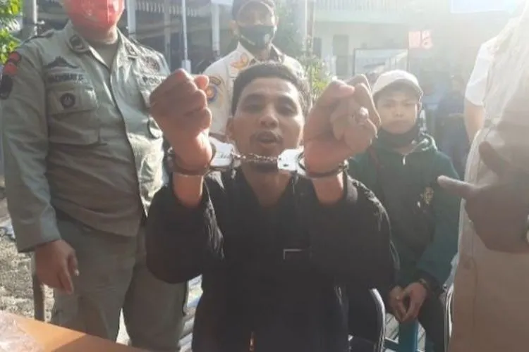 Seorang pengendara roda dua bernama Andi Albar saat memperlihatkan tangannya diborgol karena tidak mengguna masker di Jalan Raya Puncak Bogor. (Suara.com/Andi Ahmad Sulaendi)