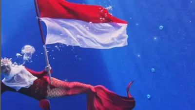 Ria Ricis mengibarkan bendera merah putih dengan menggunakan busana ekor putri duyung berwarna merah.