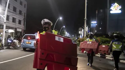 etugas kepolisian mengangkat pembatas jalan saat akan melakukan penutupan jalan dalam rangka pembatasan mobilitas warga guna menekan penyebaran COVID-19 di kawasan Bulungan, Jakarta, Senin (21/6/2021)
