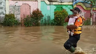 Personel BPBD Kota Bekasi mengevakuasi balita yang terdampak banjir karena tanggul Kali Bekasi di Perumahan PGP jebol, Jumat (19/2/2021).[Suara/com/Imam Faishal]