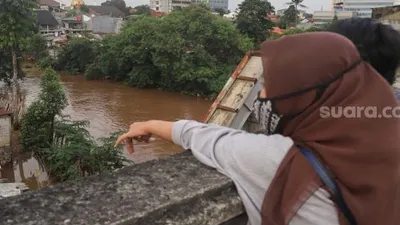 Warga menonton banjir dan aliran kali Ciliwung yang meluap dari atas Flyover Kalibata, Jakarta Selatan, Sabtu (20/2/2021). [Suara.com/Alfian Winanto]
