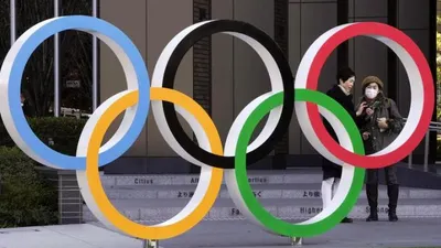 Dua orang berdiri di belakang logo Olimpiade di Tokyo, Jepang. Virus corona telah mengancam kemungkinan terselenggaranya Olimpiade 2020 di Tokyo.  (foto: EPA)