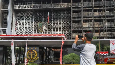 Seorang warga memfoto gedung utama Kejaksaan Agung RI yang habis terbakar di Jalan Sultan Hasanuddin, Jakarta Selatan, Minggu (23/8). [Suara.com/Alfian Winanto]