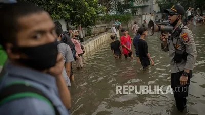Petugas kepolisian mengatur lalu lintas serta mengimbau warga untuk menjaga jarak saat banjir di Jakarta Utara.  Foto: Republika/Thoudy Badai
