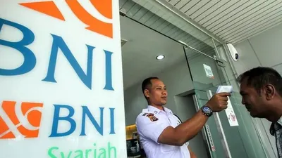 Petugas keamanan memeriksa suhu tubuh nasabah bank BNI Syariah Lhokseumawe, Aceh, Jumat (13/3/2020). (ANTARA FOTO/Rahmad/Tirto.id)