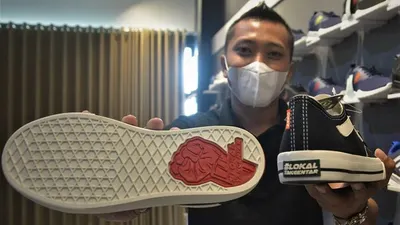 Aditya Caesarico menunjukkan sol sepatu bertuliskan #LokalTakGentar dengan genggaman tangan. Sepatu ini dijual dengan harga Rp99.900 per pasang. (Ayojakarta/Budi Cahyono)