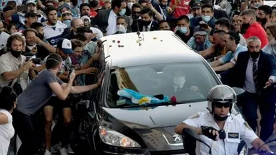 Foto yang dirilis Telam menunjukkan para penggemar berkerumun di samping mobil jenazah yang membawa mendiang legenda sepak bola Argentina Diego Armando Maradona dalam perjalanan dari istana kepresidenan Casa Rosada ke pemakaman Jardin Bella Vista, di Buenos Aires pada Kamis (26/11/2020) waktu setempat. [Raul FERRARI / TELAM / AFP]
