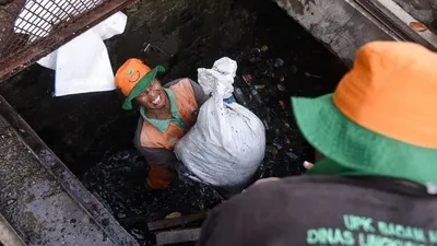 Petugas Dinas Lingkungan Hidup Pemprov DKI Jakarta mengangkat karung berisi lumpur dan sampah dari dalam salur air. (Facebook Anies Baswedan)
