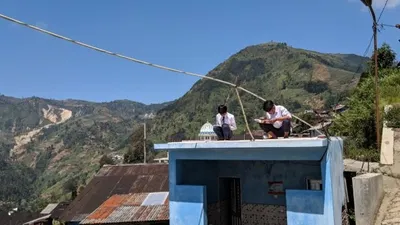 Dua orang siswa SMPN 4 Bawang saat menggunakan jaringan internet gratis yang dipasang sekolah dengan naik atap rumah. (Dok)