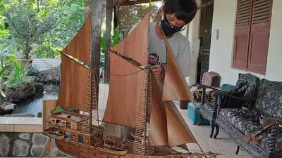 Arifin sedang merancang miniatur perahu pinisi.