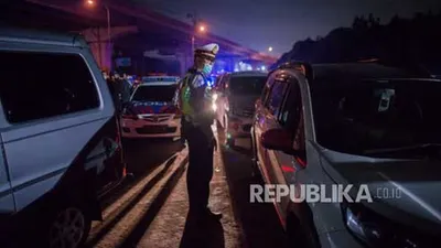 Petugas kepolisian mengarahkan kendaraan pribadi untuk keluar di Gerbang Tol Cikarang Barat, Bekasi, Jawa Barat, Sabtu (23/5) dini hari. Sekitar 200 pemudik yang menggunakan jasa travel tanpa izin beserta kendaraan pribadi terkena razia penyekatan dan akan dikembalikan ke Jakarta (Foto: Republika/Thoudy Badai )