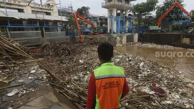 Petugas UPK Badan Air Dinas Lingkungan Hidup Provinsi DKI Jakarta dibantu alat berat mengangkat sampah kayu yang menumpuk di pintu air Manggarai, Jakarta, Selasa (22/9/2020). [Suara.com/Angga Budhiyanto]
