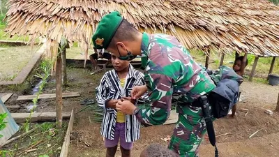 prajurit Satgas Yonif 125/Simbisa memasangkan pakaian layak pakai kepada seorang anak di  Kampung Bupul, Distrik Elikobel, Kabupaten Merauke, Provinsi Papua. (Papen Satgas Yonif 125/Simbisa, Lettu Chk Juspindeli Girsang )
