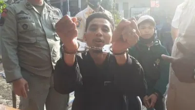 Seorang pengendara roda dua bernama Andi Albar saat memperlihatkan tangannya diborgol karena tidak mengguna masker di Jalan Raya Puncak Bogor. (Suara.com/Andi Ahmad Sulaendi)